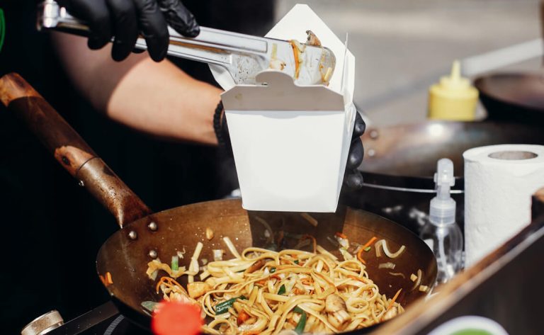 vendor placing noodles into a box from a wok
